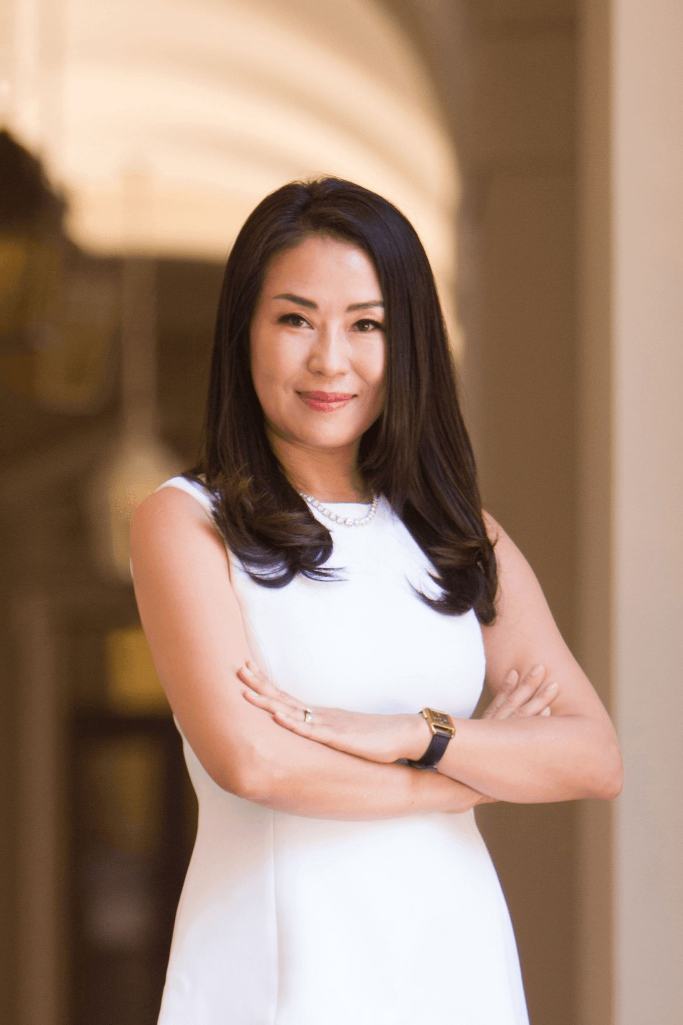 Attorney Michelle Choe in a white dress, smiling with her arms crossed in a sunlit corridor